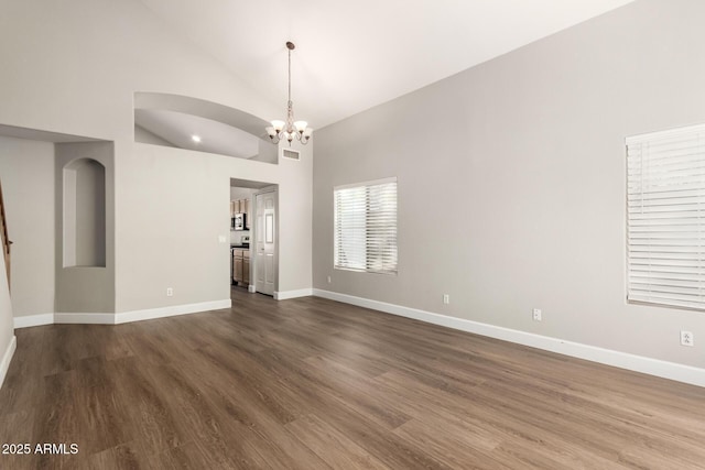 unfurnished room with dark wood-style floors, high vaulted ceiling, an inviting chandelier, and baseboards