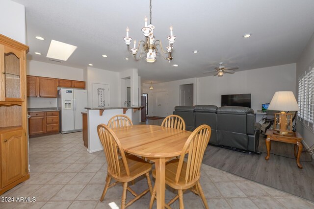 tiled dining area with ceiling fan with notable chandelier and a skylight