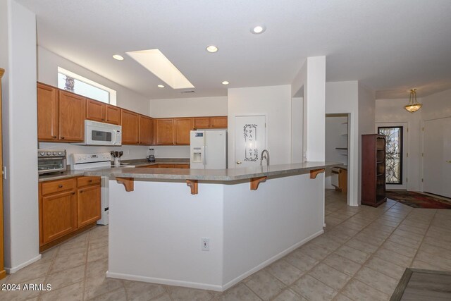 kitchen featuring white appliances, light tile patterned floors, a kitchen island with sink, and a breakfast bar