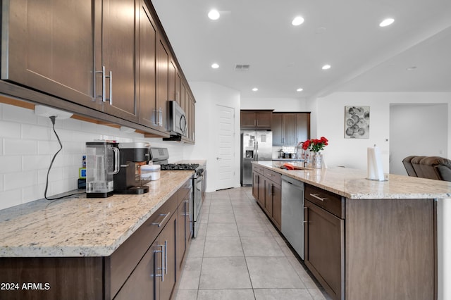 kitchen with a kitchen island with sink, light stone countertops, tasteful backsplash, light tile patterned flooring, and stainless steel appliances