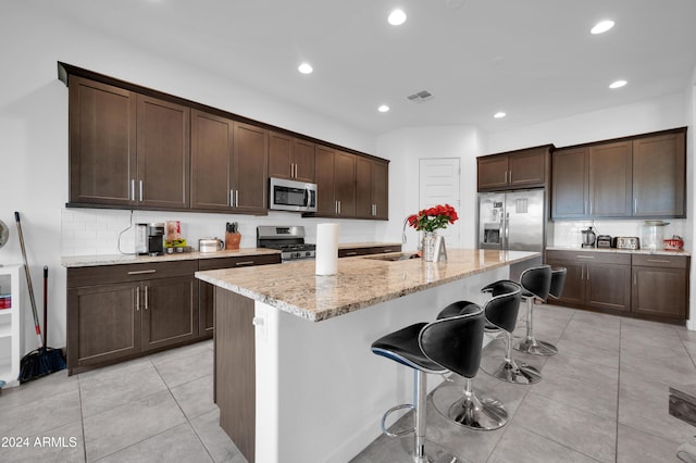 kitchen featuring a breakfast bar, sink, light stone countertops, an island with sink, and appliances with stainless steel finishes