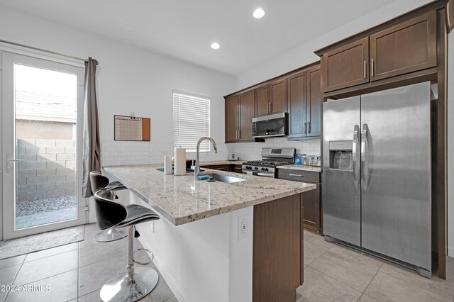 kitchen featuring sink, light stone countertops, appliances with stainless steel finishes, dark brown cabinets, and a kitchen bar