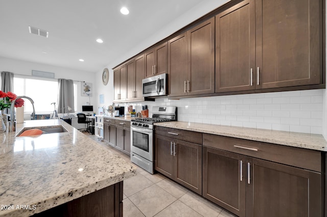 kitchen with light stone counters, sink, stainless steel appliances, and dark brown cabinets