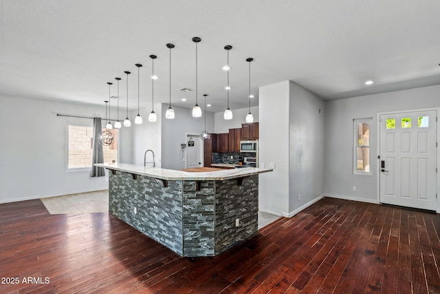 7911 E Posada Ave, Mesa, AZ 85212 - kitchen featuring stainless steel microwave, hardwood / wood-style floors, a kitchen bar, a spacious island, and decorative backsplash