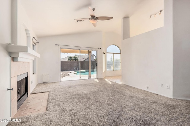 unfurnished living room featuring high vaulted ceiling, light colored carpet, a tile fireplace, and ceiling fan