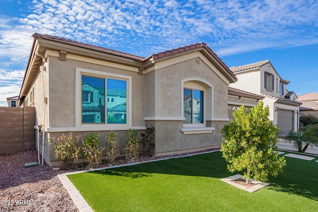 view of front of property with an attached garage, fence, a tiled roof, stucco siding, and a front lawn