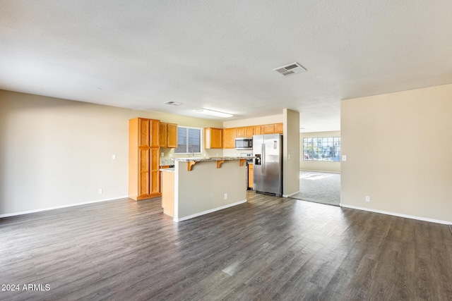 kitchen featuring a kitchen breakfast bar, a textured ceiling, stainless steel appliances, dark wood-type flooring, and a kitchen island