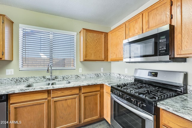 kitchen featuring sink, hardwood / wood-style flooring, a textured ceiling, appliances with stainless steel finishes, and light stone counters