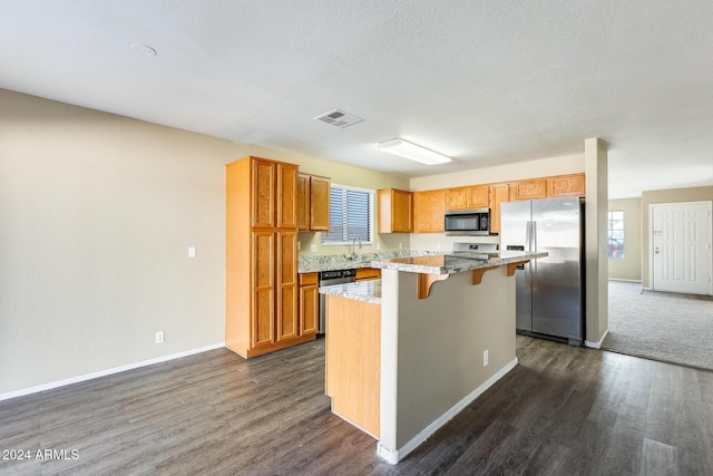 kitchen with a breakfast bar, a healthy amount of sunlight, appliances with stainless steel finishes, a kitchen island, and dark hardwood / wood-style flooring