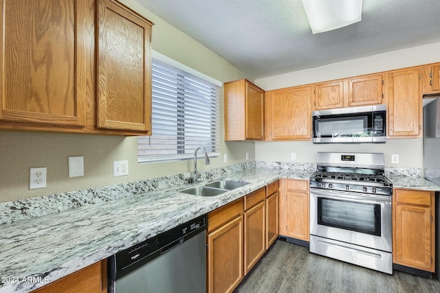 kitchen with sink, stainless steel appliances, light stone counters, dark hardwood / wood-style floors, and a textured ceiling