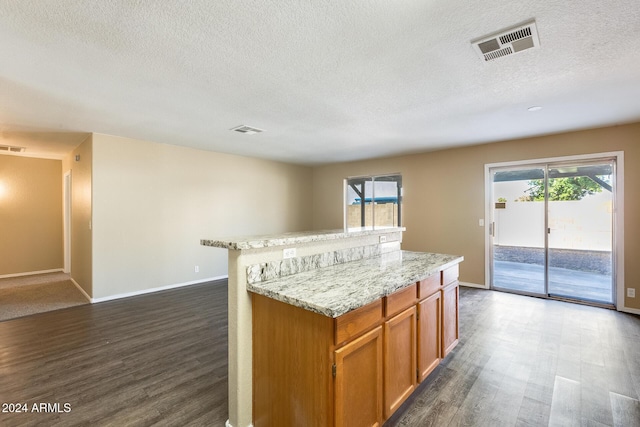 kitchen with a textured ceiling, a kitchen island, a wealth of natural light, and dark wood-type flooring