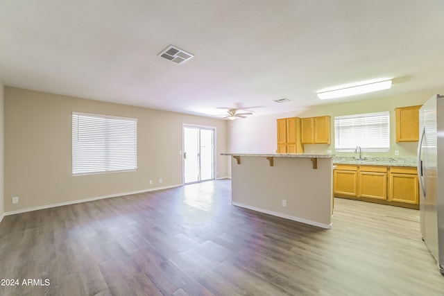 kitchen with light wood-type flooring, light stone counters, a center island, stainless steel refrigerator, and a breakfast bar area