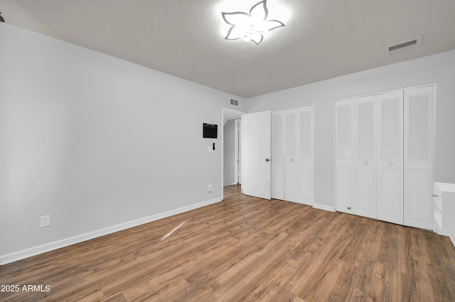 unfurnished bedroom with multiple closets, hardwood / wood-style floors, and a textured ceiling