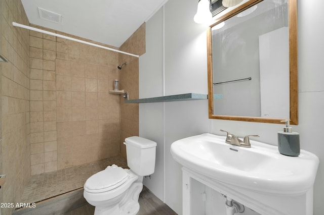 bathroom with tiled shower, toilet, and sink