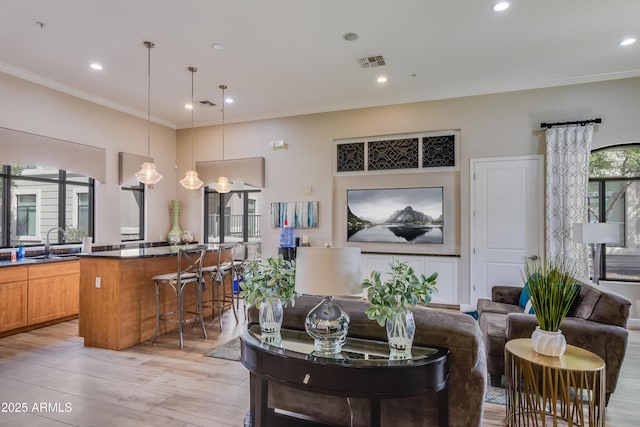 living area with light wood-style flooring, visible vents, recessed lighting, and crown molding