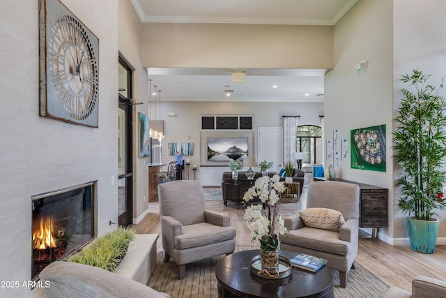 living area featuring wood finished floors, a fireplace, crown molding, baseboards, and a towering ceiling