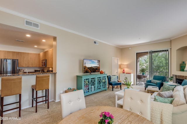 living area with a fireplace, light colored carpet, visible vents, and ornamental molding