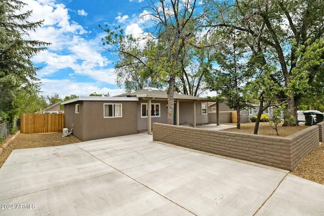 view of front of property with stucco siding, a patio, and fence