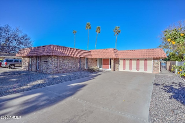 single story home featuring mansard roof, an attached garage, brick siding, a tile roof, and concrete driveway