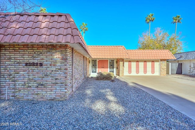 view of front of property featuring an attached garage, a tile roof, concrete driveway, and brick siding