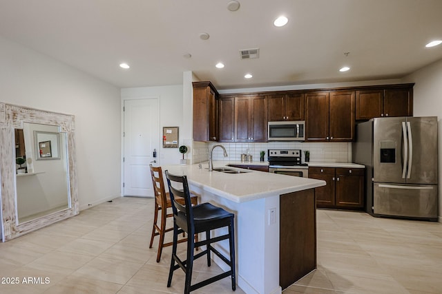 kitchen featuring dark brown cabinets, a sink, stainless steel appliances, a kitchen bar, and visible vents