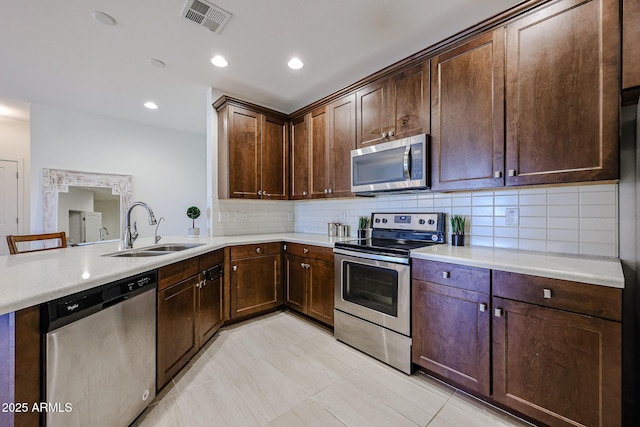 kitchen featuring a sink, stainless steel appliances, a peninsula, tasteful backsplash, and visible vents
