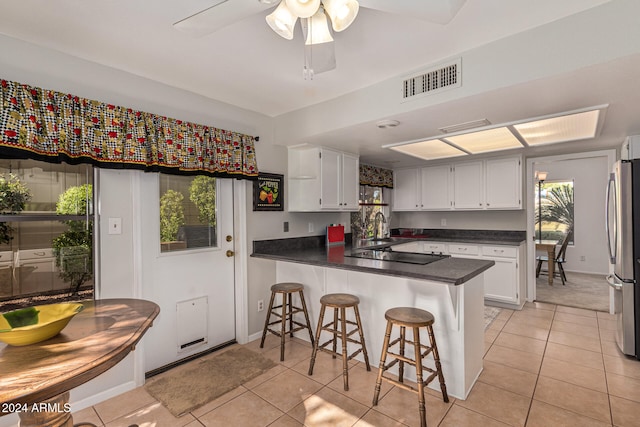 kitchen with white cabinetry, kitchen peninsula, light tile patterned floors, and stainless steel refrigerator