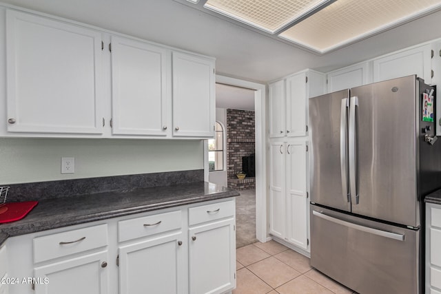 kitchen featuring white cabinets, dark stone counters, light tile patterned floors, and stainless steel refrigerator