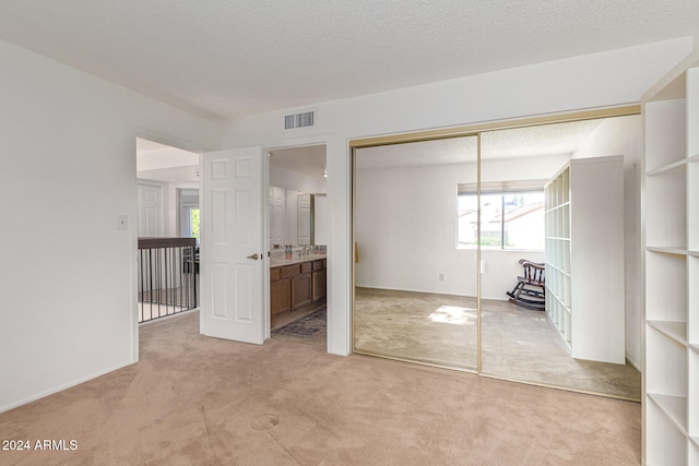 unfurnished bedroom featuring ensuite bathroom, light colored carpet, a textured ceiling, and a closet