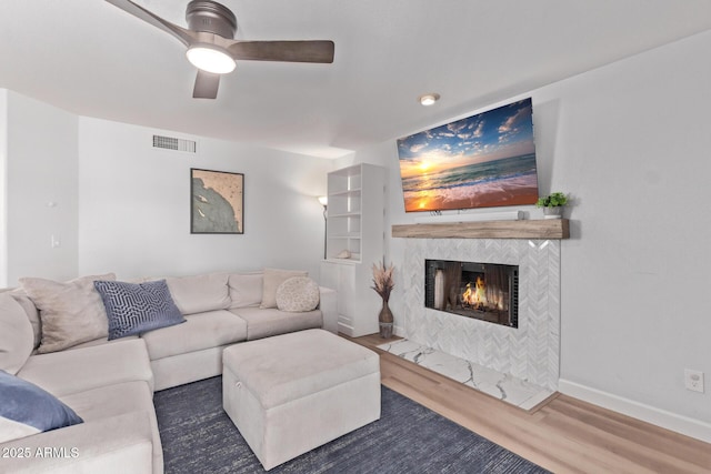 living room featuring ceiling fan, visible vents, a tiled fireplace, wood finished floors, and baseboards
