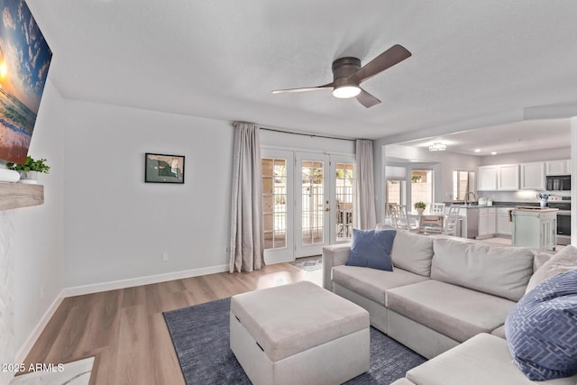 living area featuring french doors, a ceiling fan, light wood-style flooring, and baseboards