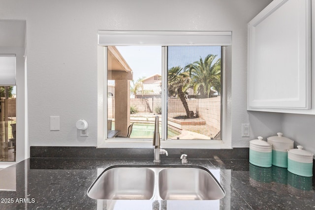 interior details with a sink, white cabinets, and dark stone countertops