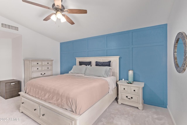 bedroom with ceiling fan, light colored carpet, a decorative wall, lofted ceiling, and visible vents