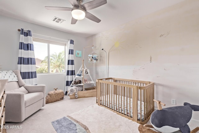 carpeted bedroom featuring a nursery area, ceiling fan, and visible vents