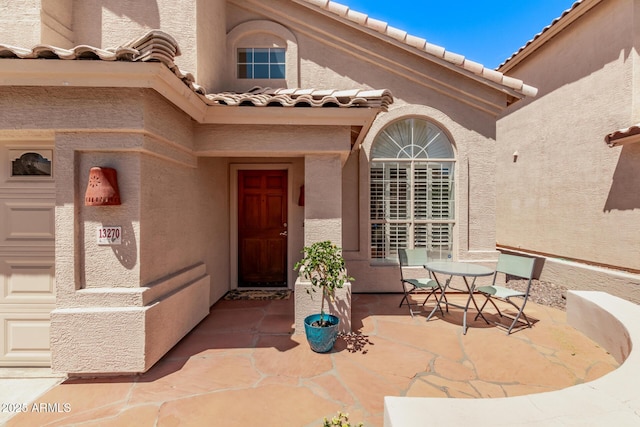 entrance to property featuring a patio area, stucco siding, a tile roof, and outdoor dining space