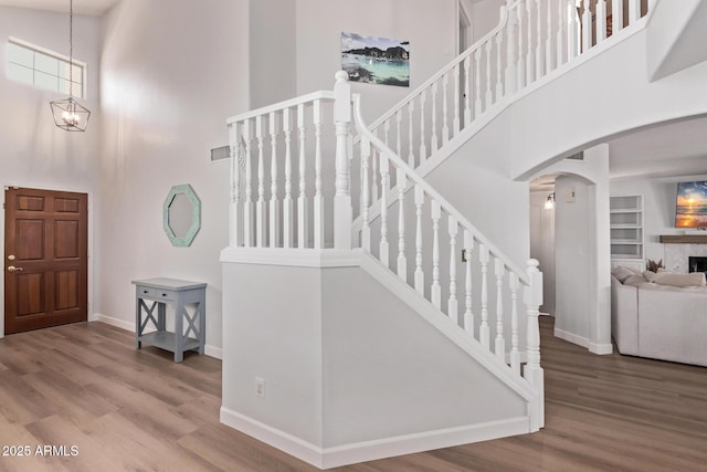 entryway featuring a towering ceiling, wood finished floors, a fireplace, baseboards, and arched walkways