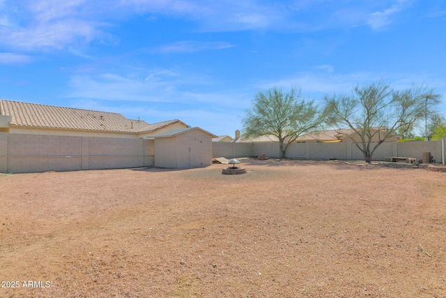 view of yard featuring an outdoor structure, a fenced backyard, a storage shed, and an outdoor fire pit