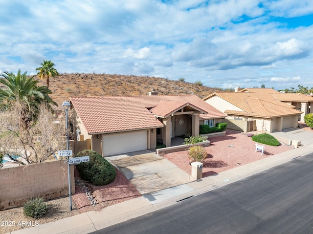 view of front of house with fence, a tiled roof, stucco siding, driveway, and an attached garage