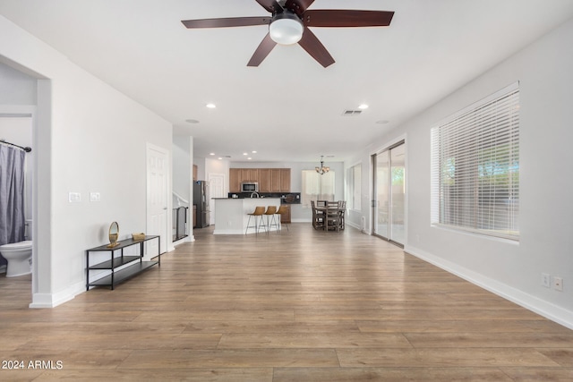 unfurnished living room with ceiling fan with notable chandelier and light hardwood / wood-style floors