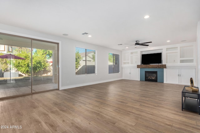 unfurnished living room with wood-type flooring, built in features, and ceiling fan