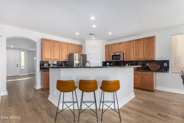 kitchen featuring a center island with sink, appliances with stainless steel finishes, wood-type flooring, and backsplash