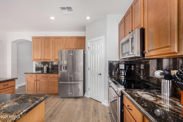 kitchen with backsplash, stainless steel appliances, light hardwood / wood-style flooring, and dark stone counters