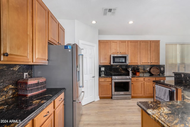 kitchen with appliances with stainless steel finishes, light hardwood / wood-style flooring, dark stone counters, and backsplash