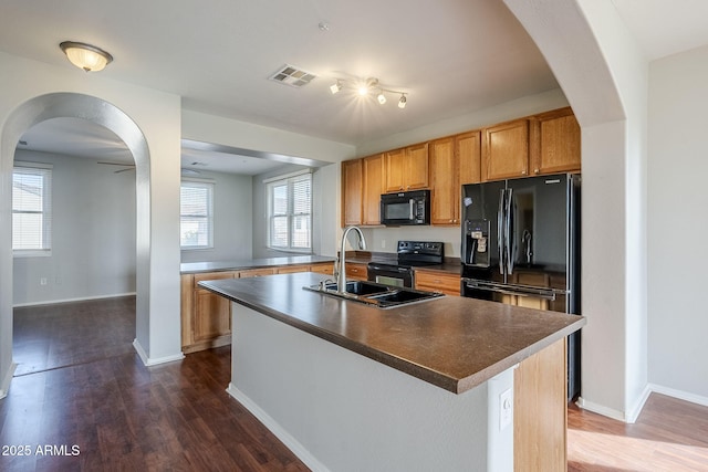 kitchen with dark wood-type flooring, a center island with sink, black appliances, and sink