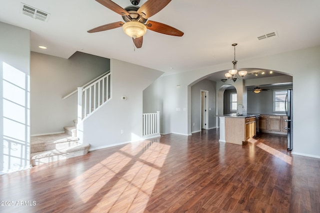 unfurnished living room with sink, dark wood-type flooring, and ceiling fan with notable chandelier