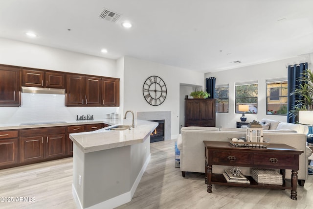 kitchen with visible vents, a glass covered fireplace, a sink, under cabinet range hood, and black electric cooktop