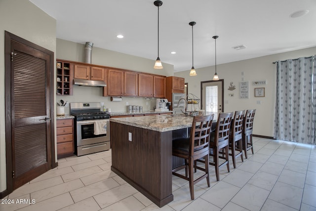 kitchen with gas stove, light stone countertops, hanging light fixtures, an island with sink, and a breakfast bar