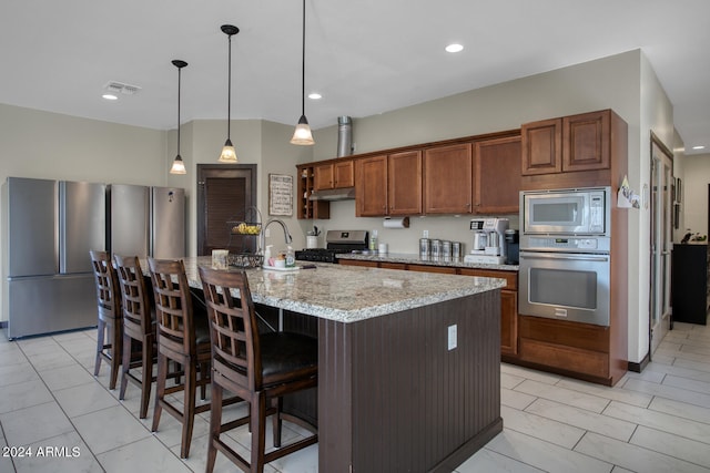 kitchen featuring a center island with sink, sink, appliances with stainless steel finishes, light stone countertops, and decorative light fixtures