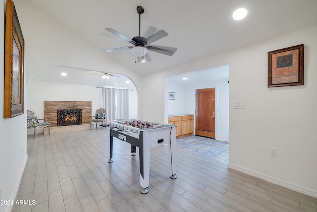 recreation room with a stone fireplace, light wood-type flooring, lofted ceiling, and ceiling fan