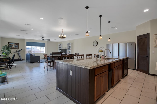 kitchen with an island with sink, light stone countertops, sink, and decorative light fixtures